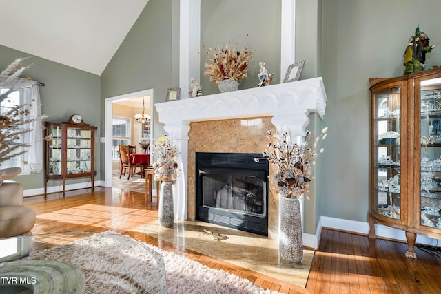 living area featuring a fireplace, high vaulted ceiling, baseboards, and hardwood / wood-style floors