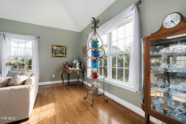 living area with baseboards, plenty of natural light, hardwood / wood-style floors, and vaulted ceiling