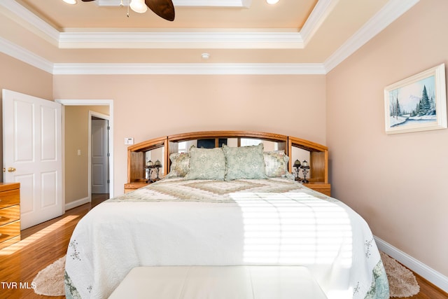 bedroom with crown molding, wood finished floors, baseboards, and a raised ceiling