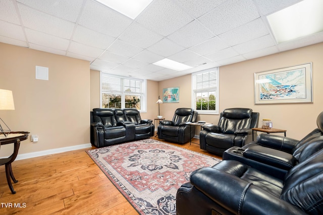 living area with light wood-type flooring, a drop ceiling, and baseboards