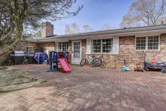 back of property with a patio area, brick siding, and a chimney