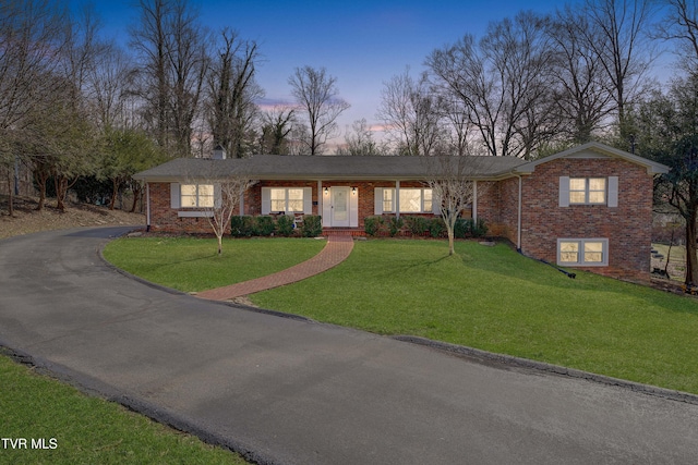 view of front of home featuring brick siding, aphalt driveway, and a yard