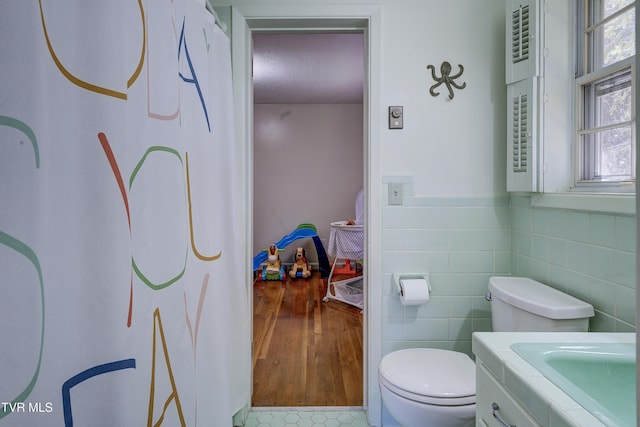 bathroom with toilet, tile walls, wainscoting, and vanity