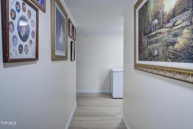 hallway with an accent wall, light wood-style floors, and baseboards