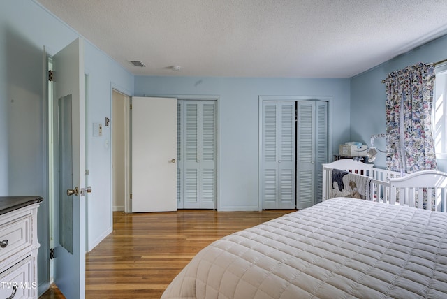 bedroom featuring baseboards, a textured ceiling, multiple closets, and wood finished floors