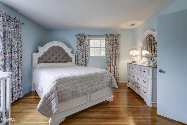 bedroom featuring visible vents, baseboards, a textured ceiling, and wood finished floors