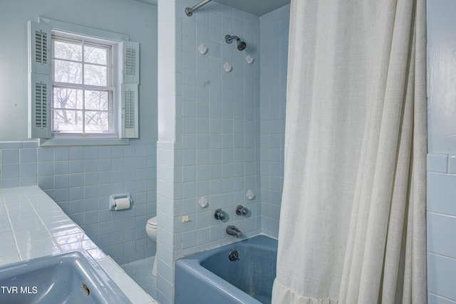 full bath featuring shower / bathtub combination with curtain, toilet, tile walls, and wainscoting