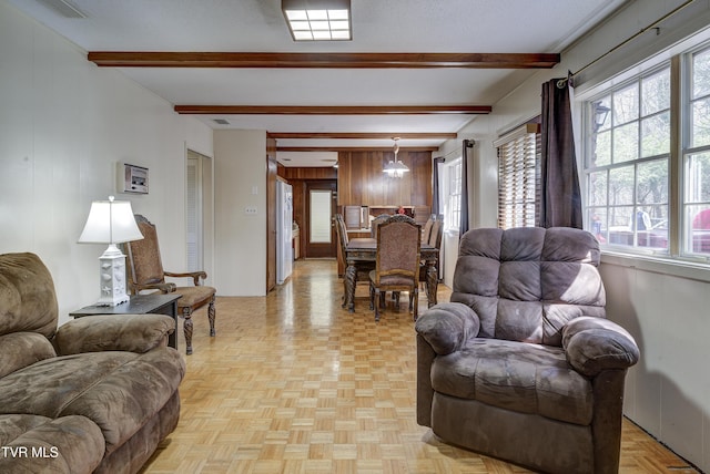 living area featuring beam ceiling, wooden walls, and a textured ceiling