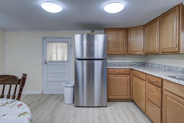 kitchen featuring light wood-style flooring, brown cabinetry, and freestanding refrigerator