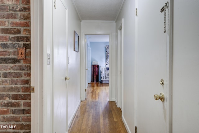 hall featuring ornamental molding, a textured ceiling, wood finished floors, brick wall, and baseboards