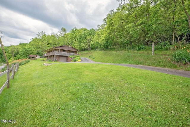 view of yard with aphalt driveway, a garage, fence, and a wooded view