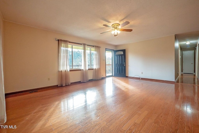 empty room with a ceiling fan, visible vents, baseboards, light wood-style floors, and a textured ceiling