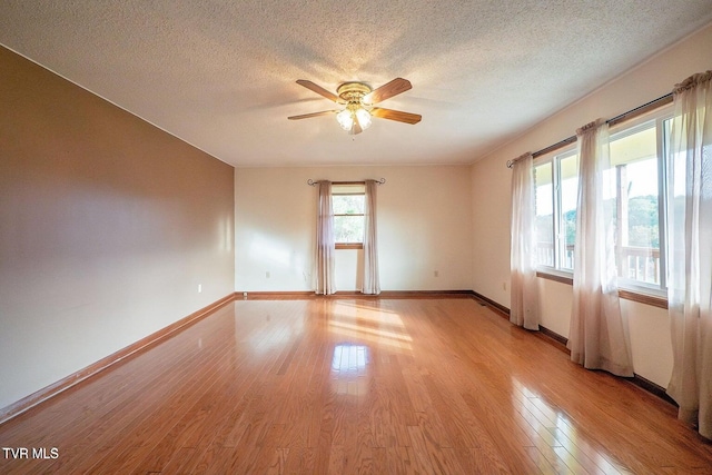 empty room with a ceiling fan, baseboards, light wood-type flooring, and a textured ceiling