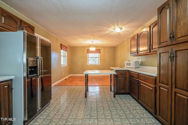 kitchen with black fridge, decorative light fixtures, light floors, light countertops, and white microwave