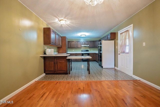 kitchen with baseboards, light wood finished floors, a peninsula, freestanding refrigerator, and extractor fan