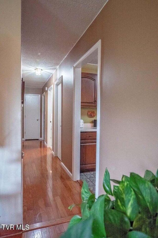 corridor with light wood-style floors and a textured ceiling