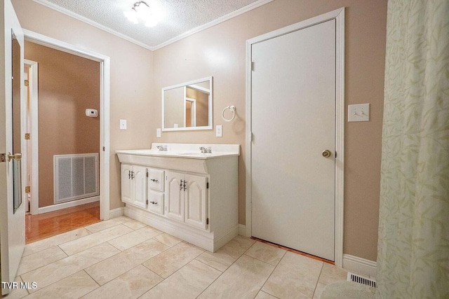 bathroom with visible vents, a textured ceiling, crown molding, and double vanity