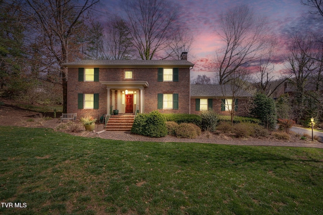 colonial home featuring brick siding, a chimney, and a front yard