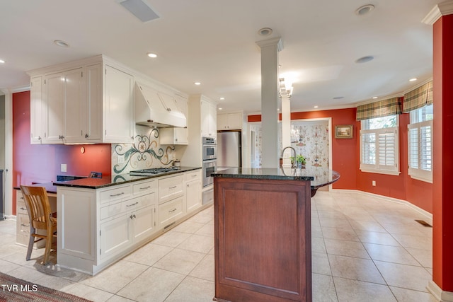 kitchen featuring white cabinets, light tile patterned flooring, decorative columns, tasteful backsplash, and under cabinet range hood