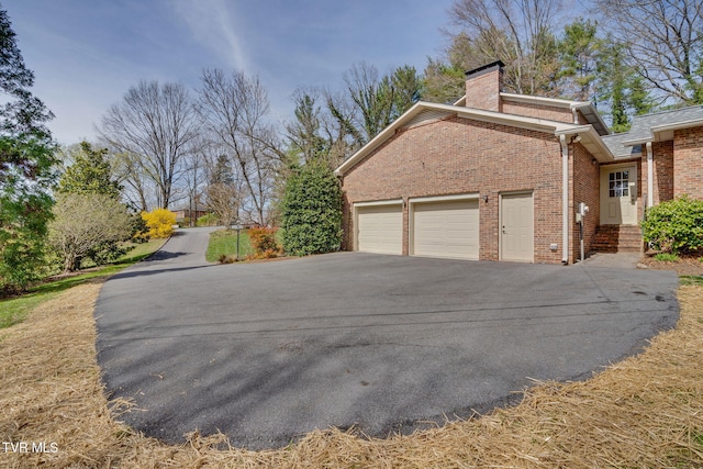 view of side of home with a garage, a chimney, driveway, and brick siding