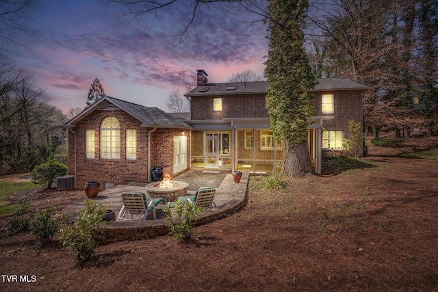 back of property at dusk featuring a patio, a chimney, brick siding, an outdoor fire pit, and central air condition unit