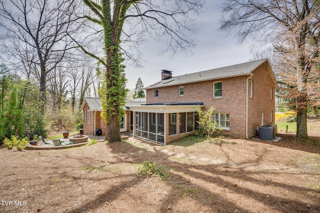 rear view of house with a chimney, a sunroom, central air condition unit, brick siding, and an outdoor fire pit