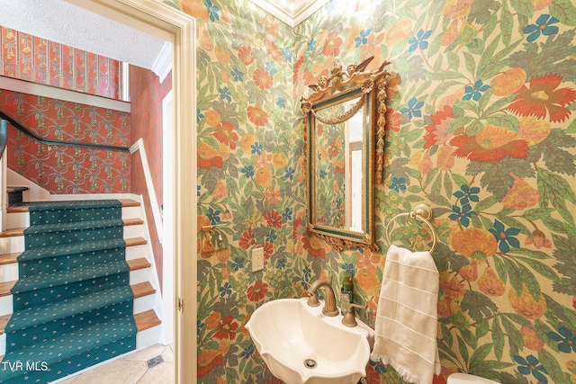 half bathroom with tile patterned flooring, a sink, and wallpapered walls