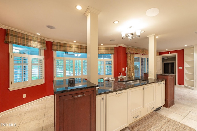 kitchen with white cabinets, a sink, dark stone counters, light tile patterned floors, and ornamental molding