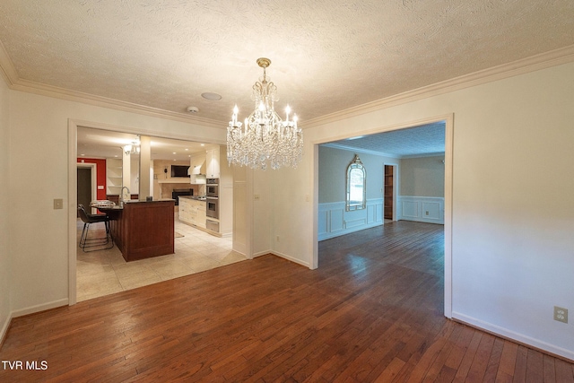 unfurnished dining area with crown molding, a textured ceiling, an inviting chandelier, and light wood-type flooring