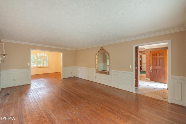 spare room featuring an inviting chandelier, a textured ceiling, a wainscoted wall, hardwood / wood-style floors, and visible vents