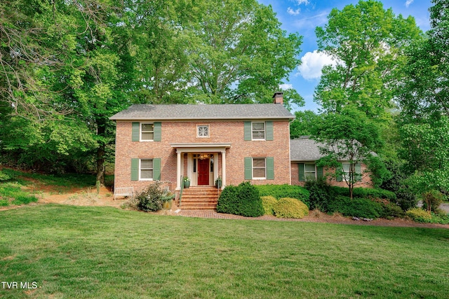 colonial-style house with a chimney, brick siding, and a front yard