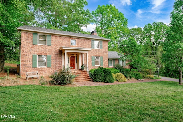 colonial home featuring brick siding, a front lawn, and a chimney
