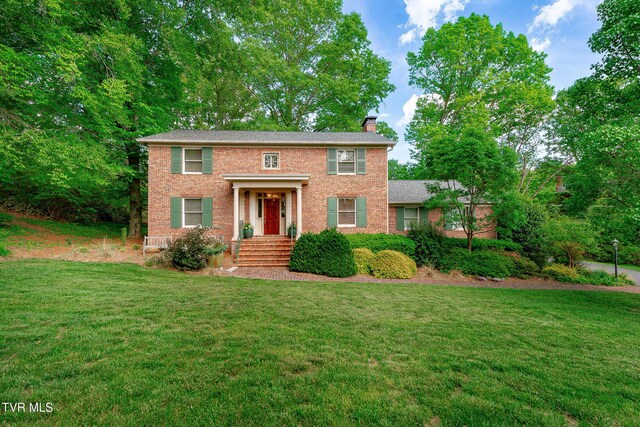 colonial home featuring brick siding, a chimney, and a front lawn
