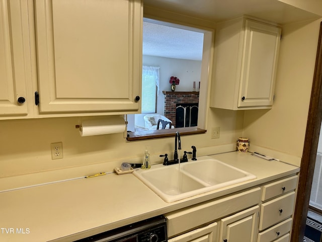 kitchen with a sink, a brick fireplace, white cabinets, and light countertops