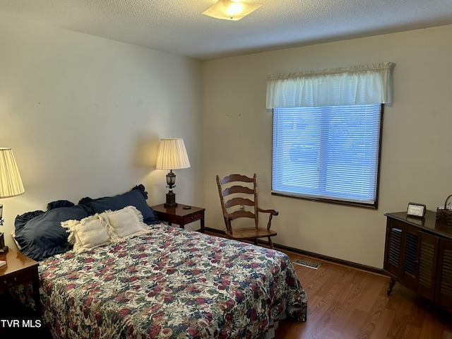 bedroom with visible vents, baseboards, a textured ceiling, and wood finished floors