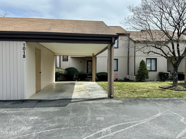 townhome / multi-family property with an attached carport, a front lawn, driveway, and a shingled roof