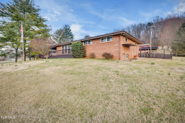 exterior space featuring brick siding, a wooden deck, a yard, and fence