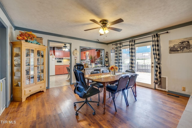 dining space with light wood finished floors, visible vents, a textured ceiling, and crown molding