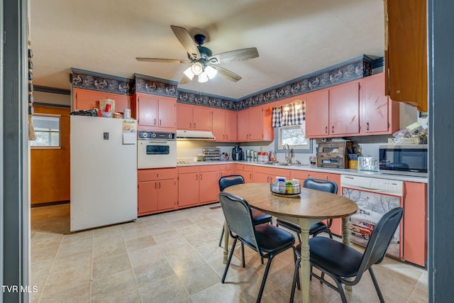 kitchen featuring a ceiling fan, under cabinet range hood, a sink, white appliances, and light countertops