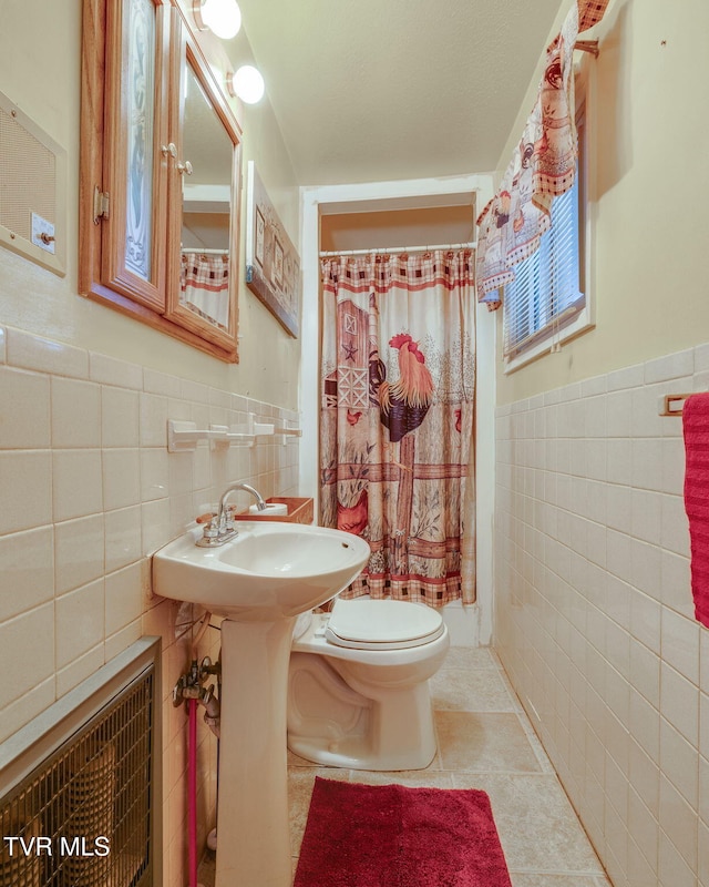 full bathroom featuring a shower with curtain, a wainscoted wall, tile walls, toilet, and tile patterned floors