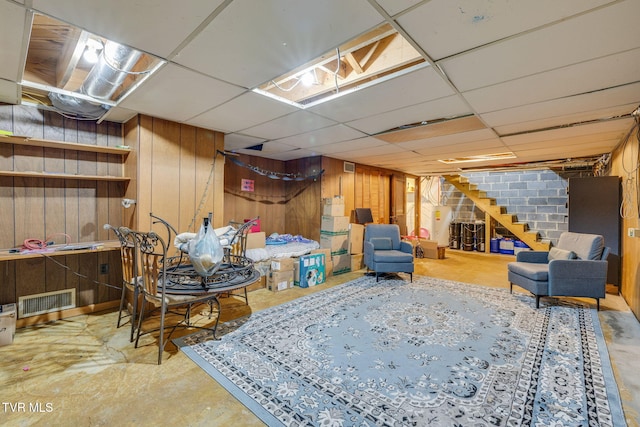 finished basement featuring visible vents, stairway, wooden walls, and a drop ceiling