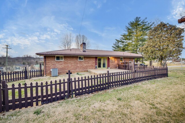 back of house featuring brick siding, fence private yard, a chimney, a yard, and a patio