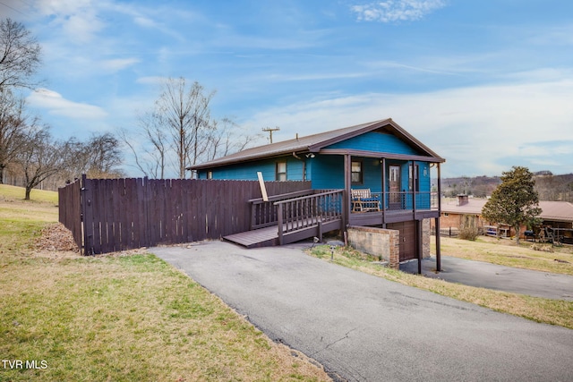 view of front of house featuring a front yard, covered porch, driveway, and fence