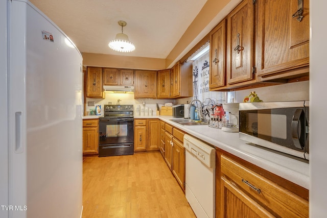 kitchen with brown cabinets, under cabinet range hood, white appliances, light wood-style floors, and light countertops