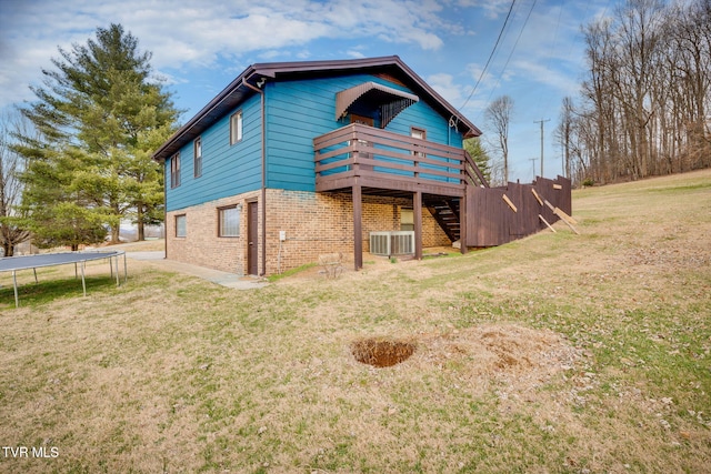 rear view of property with stairway, a yard, a deck, a trampoline, and brick siding