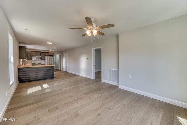 unfurnished living room with visible vents, light wood-style floors, baseboards, and a sink