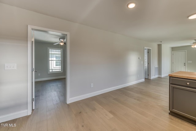 empty room featuring visible vents, a ceiling fan, light wood-type flooring, and baseboards