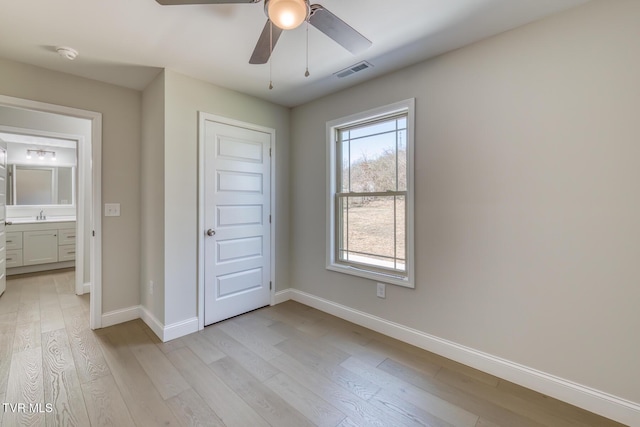 unfurnished bedroom featuring a ceiling fan, visible vents, baseboards, light wood finished floors, and a sink