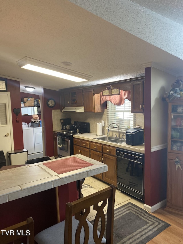 kitchen with a sink, light countertops, stainless steel range with electric stovetop, black dishwasher, and washer and dryer