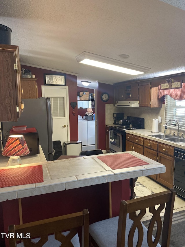 kitchen featuring a breakfast bar, a sink, stainless steel appliances, under cabinet range hood, and washer and clothes dryer